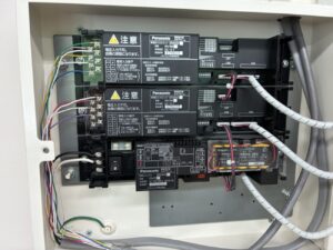 病院の消防設備点検でスプリネクス警報表示盤の蓄電池電圧を測定する様子